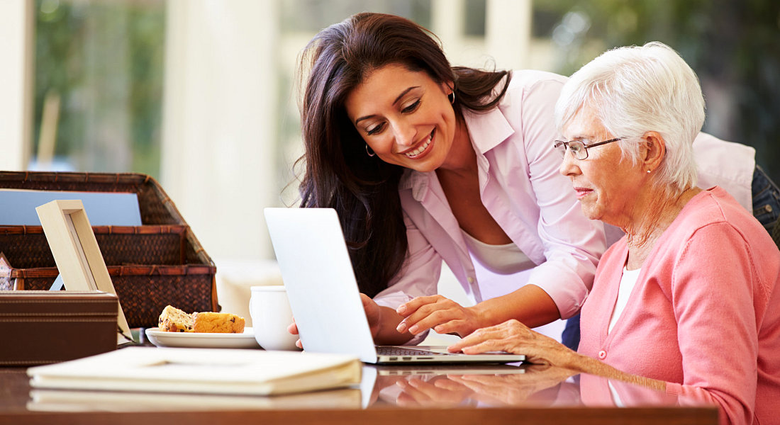 Caregiver assisting an old woman to use a laptop